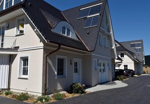 A two-story house with a sloped roof, solar panels, and a small garden area.