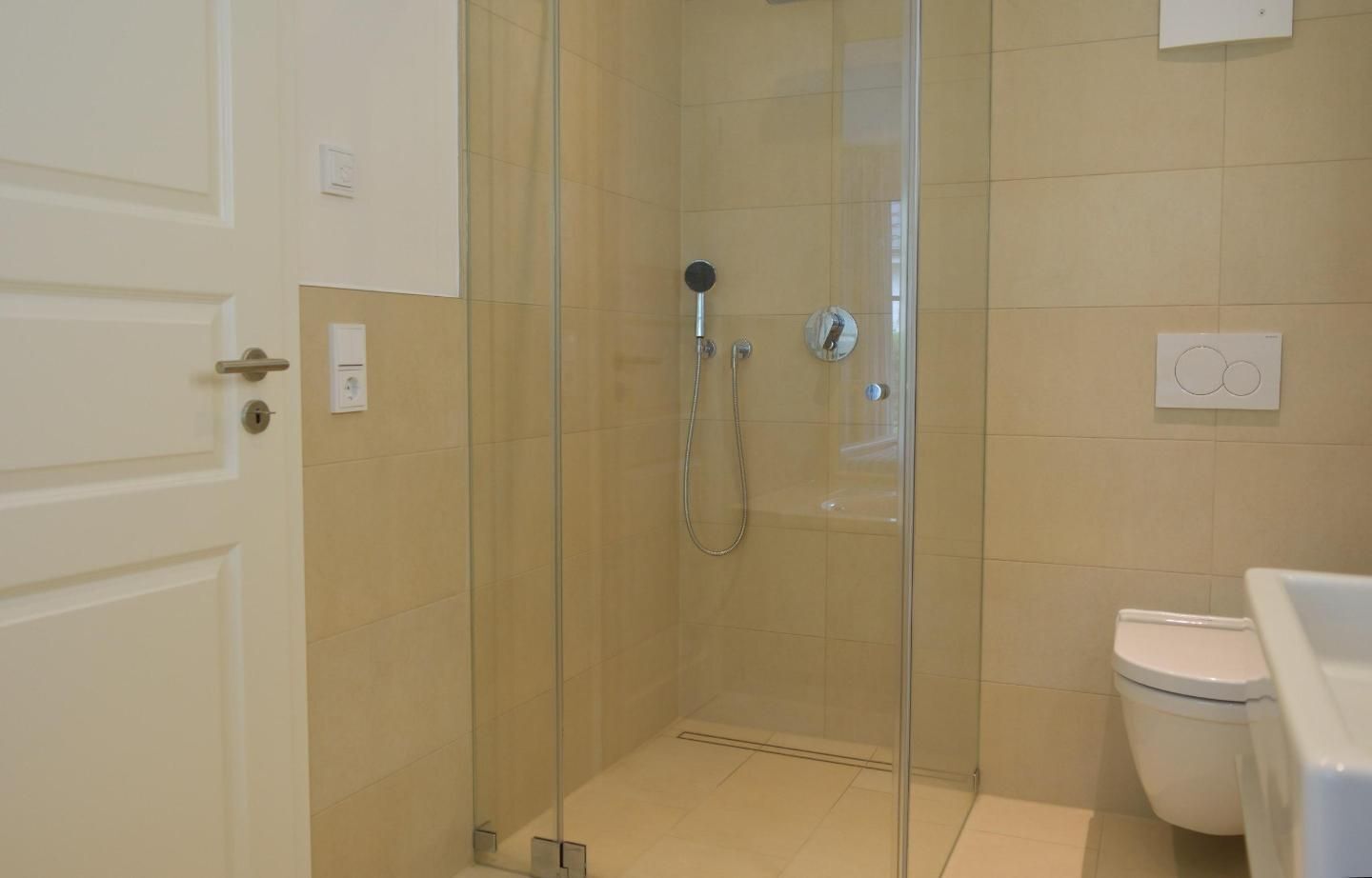 A bathroom with a glass-enclosed shower, a toilet, and a sink.