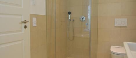 A bathroom with a glass-enclosed shower, a toilet, and a sink.