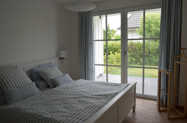 A bedroom with a large bed, a nightstand, a lamp, and a view of a garden through a sliding glass door.