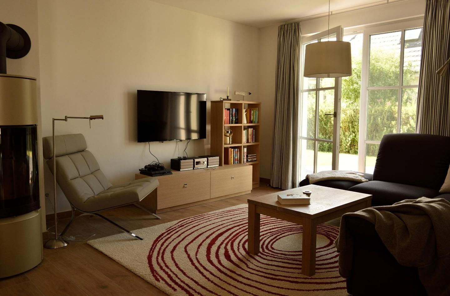 A modern living room with a flat-screen TV, a bookshelf, a comfortable sofa, and a large window with curtains.