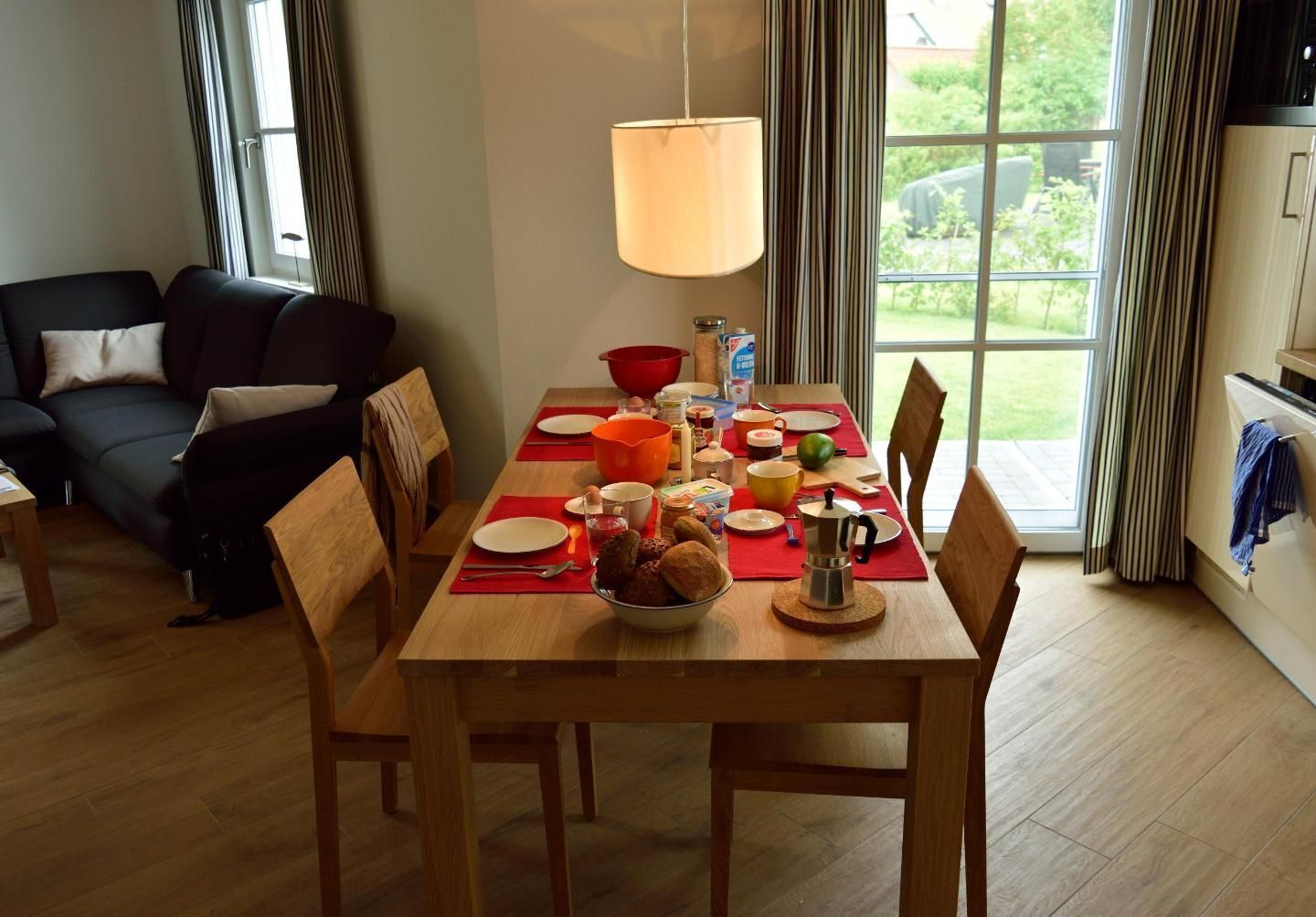 Un'area pranzo con un tavolo di legno apparecchiato per quattro persone, circondato da sedie. Un'ampia finestra offre una vista sull'esterno.