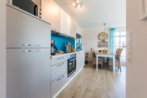 A modern kitchen with white cabinets, a coffee maker, and a dining area with wicker chairs and a table.