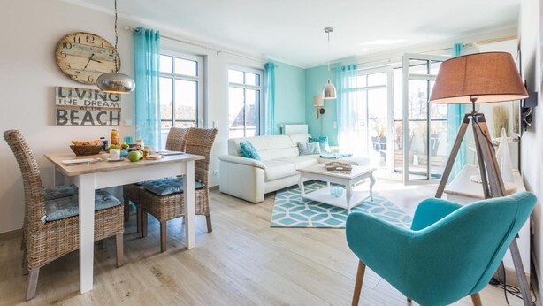 Un salón luminoso con un sofá blanco, sillones color turquesa y un comedor con sillas de mimbre.
