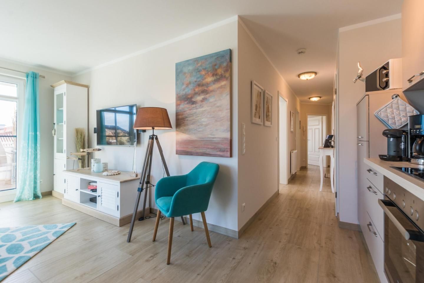 A modern living room with a teal chair, a floor lamp, and a painting on the wall.