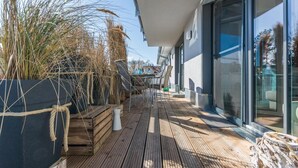 Una terraza de madera con mobiliario exterior y plantas en macetas.