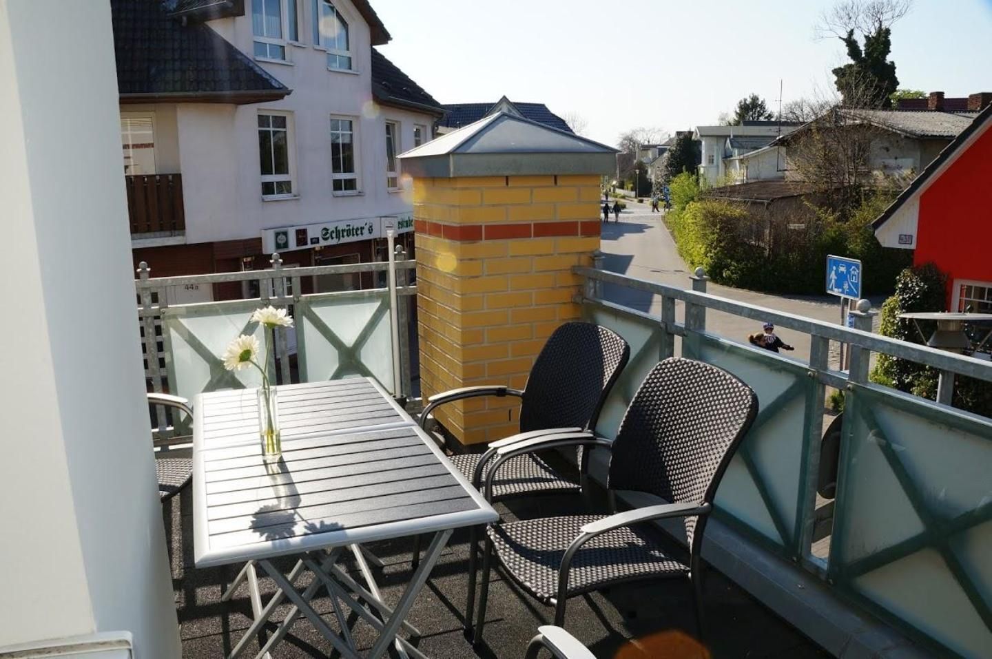 Ein Balkon mit Tisch und Stühlen, einer Blumenvase und einem Gebäude mit einem Schild im Hintergrund.