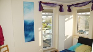 Un dormitorio con cama, una silla, ventana con vistas y un cuadro en la pared.