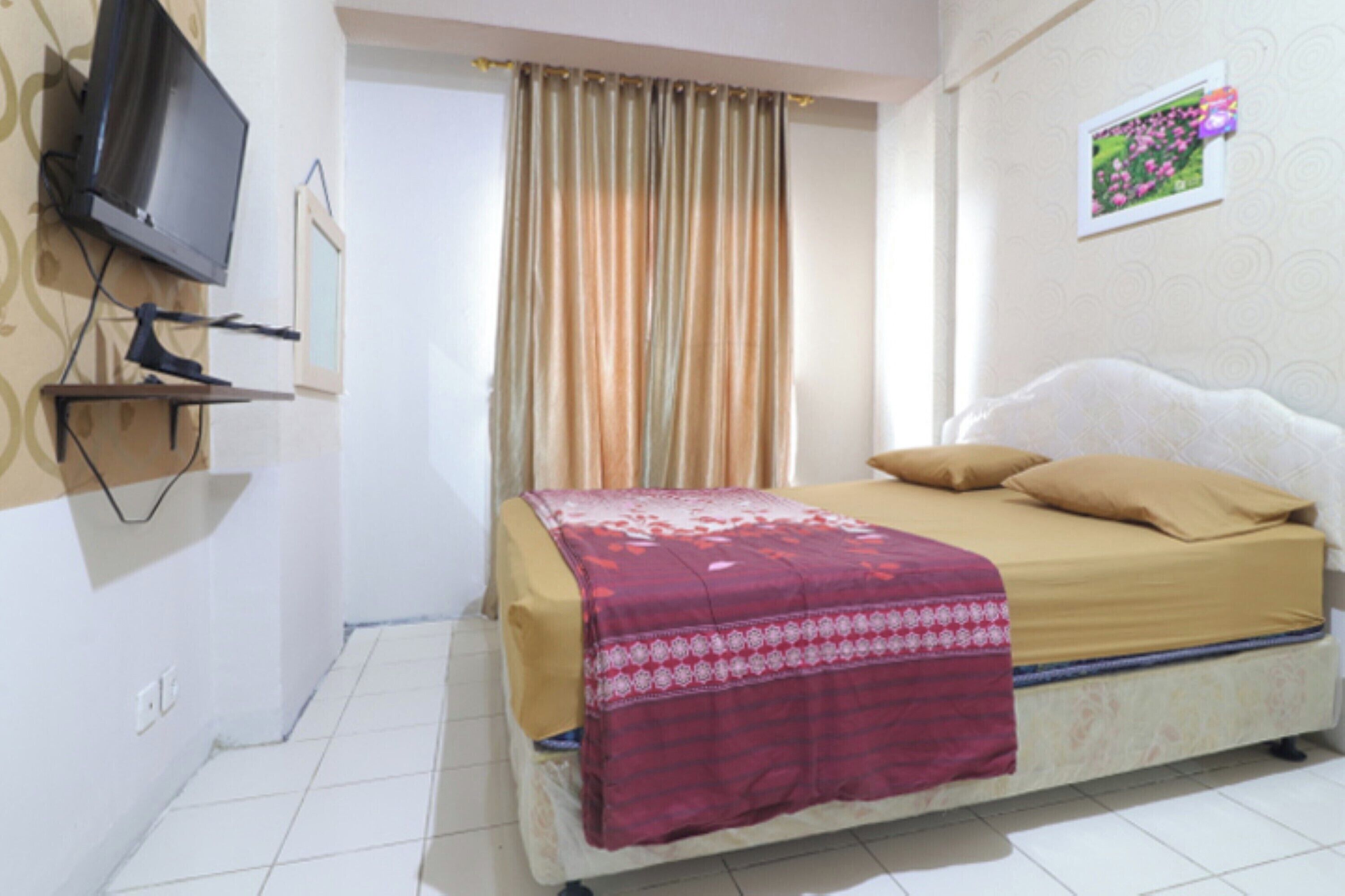 A bedroom with a bed, a television mounted on the wall, and a window with curtains.