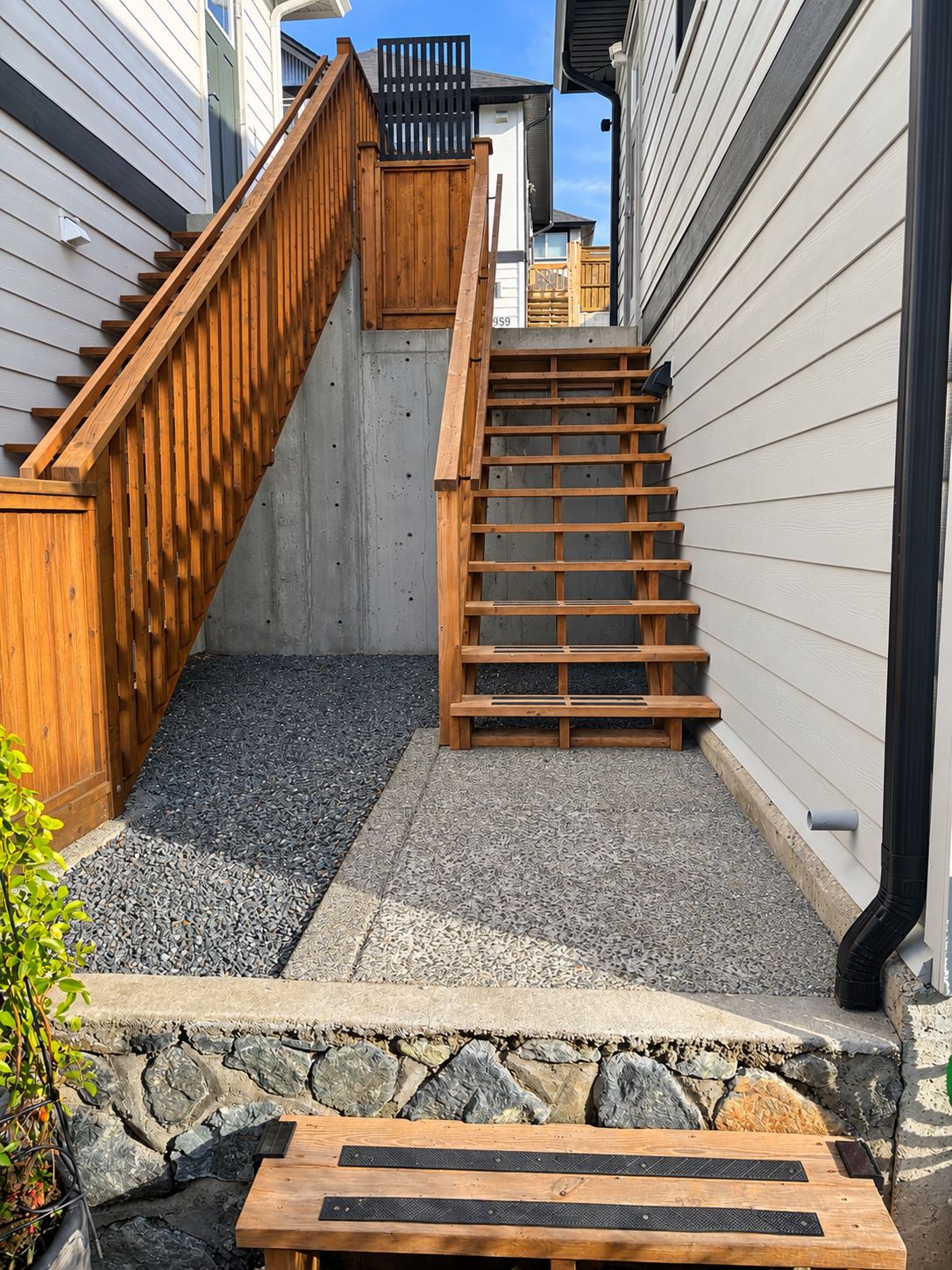 A wooden staircase leading to a house with a stone foundation and a metal gutter.