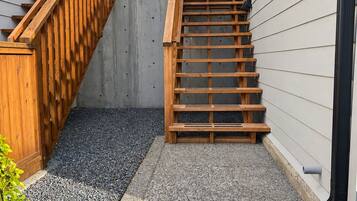 A wooden staircase leading to a house with a stone foundation and a metal gutter.