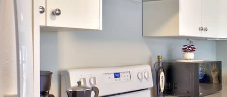 Une cuisine avec des meubles blancs, une cuisinière, un four à micro-ondes et une machine à café.