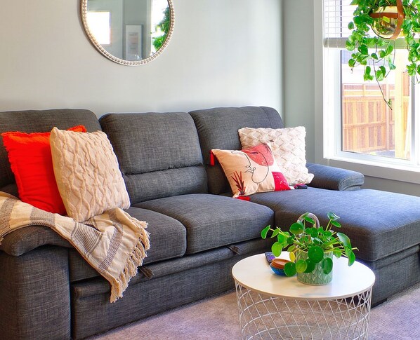 A modern living room with a grey sofa, red and beige cushions, a white coffee table with a plant, and a hanging plant.