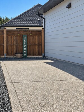 A garage door with a 'WELCOME' sign, a wooden fence, and a gravel driveway. - Zen Mountaire retreat, 1 bedroom, 1 bath, private parking (Langford)