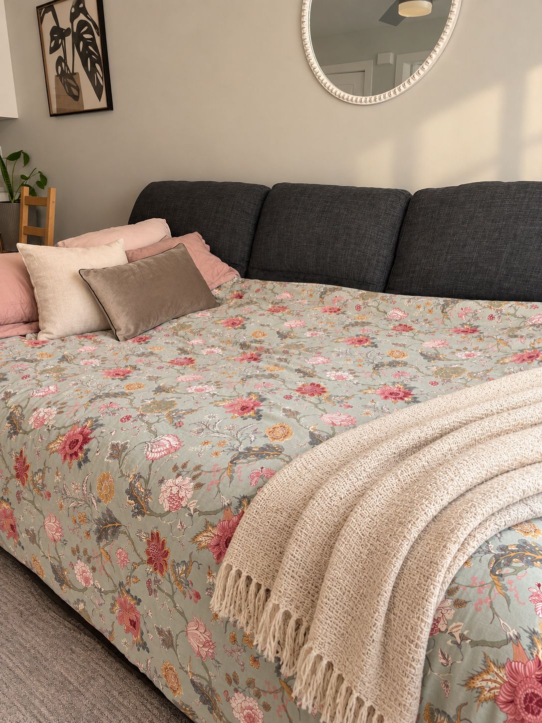 A bedroom with a floral bedspread, a large mirror, and a bedside table with a plant.