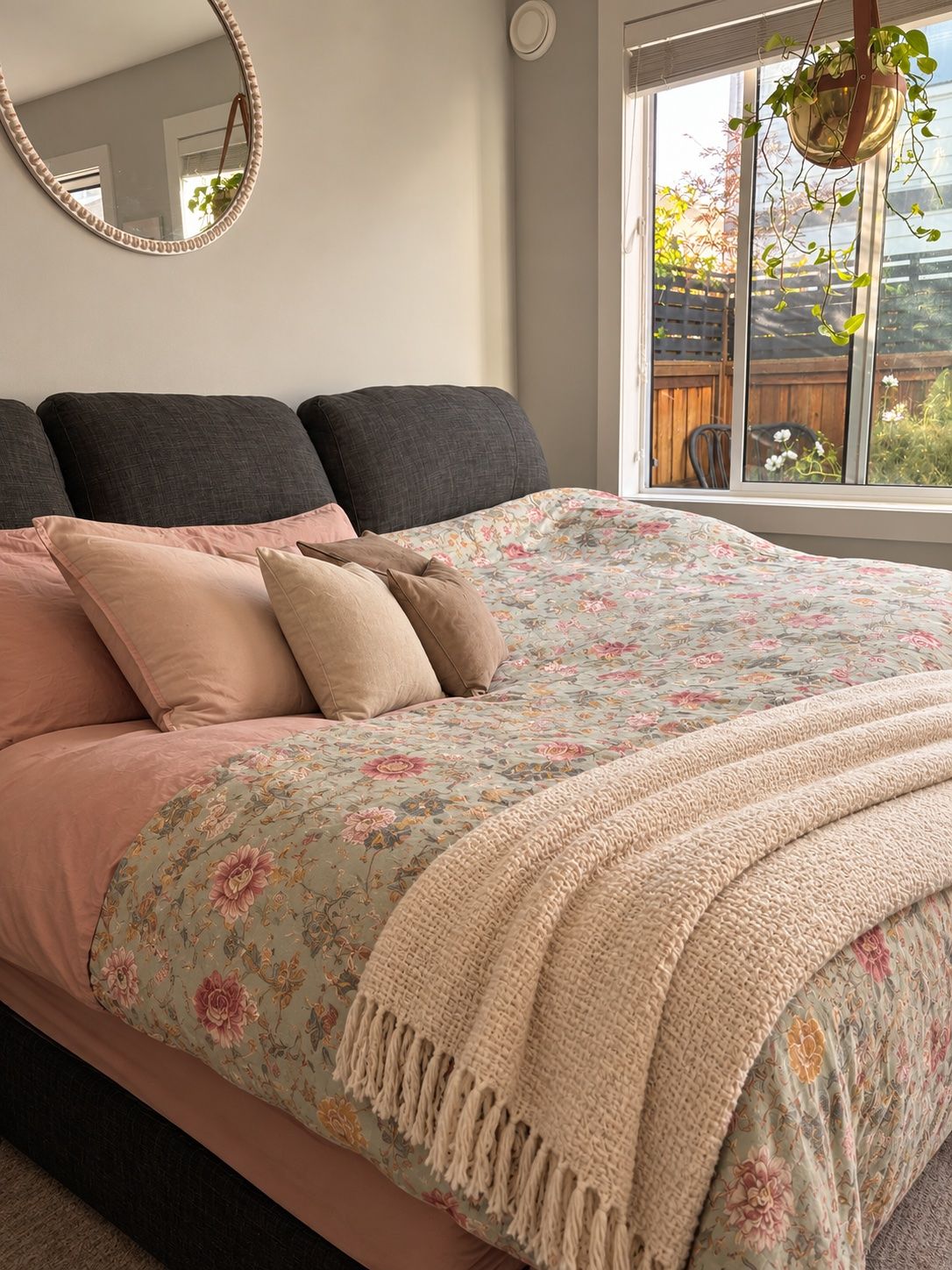 A bed with a floral duvet, multiple pillows, and a knitted throw.