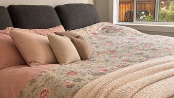 A bed with a floral duvet, multiple pillows, and a knitted throw.