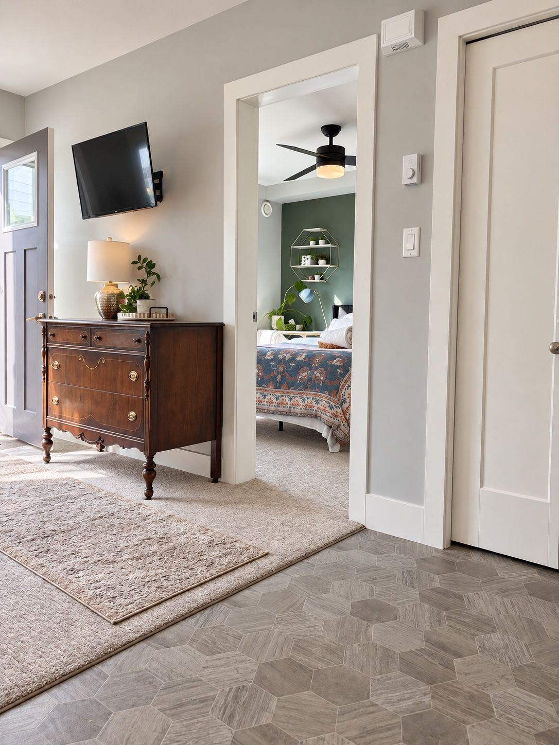 Une chambre avec une commode en bois, un téléviseur à écran plat, un lit recouvert d’une couvre-lit à motifs floraux et un ventilateur de plafond.