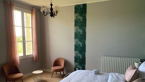 Una camera da letto con un letto, due poltrone, un tavolino rotondo, un lampadario e una finestra con tende.