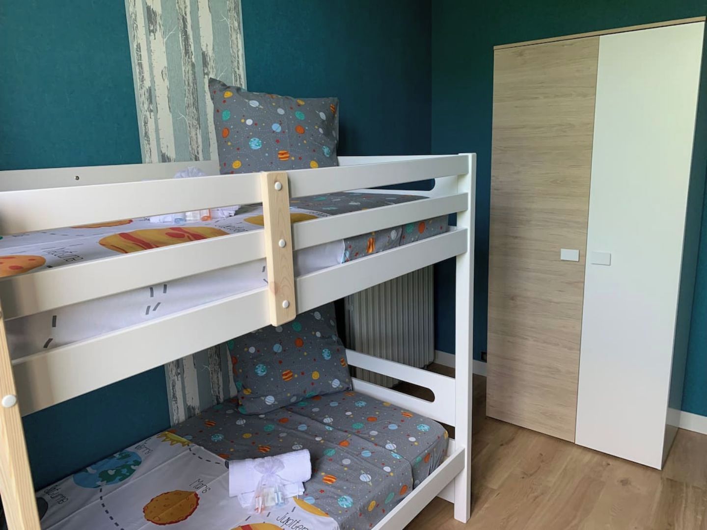 Un lit superposé avec une housse de matelas sur le thème de l’espace, une tête de lit en bois et un seul oreiller.