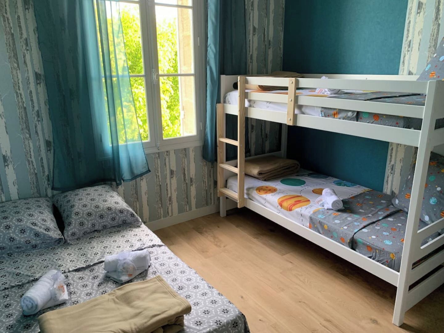 A room with a bunk bed, a single bed, and a window with curtains.