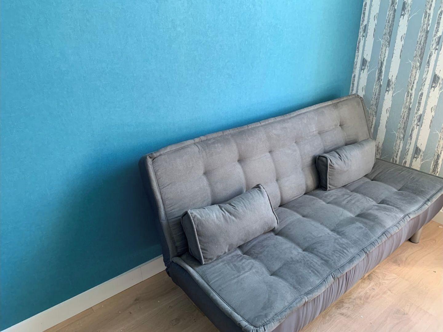 A grey sofa against a blue wall with a vertical striped pattern.