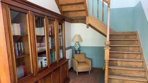 Una scala in legno con una sedia color beige e una libreria in una stanza con pavimento piastrellato.