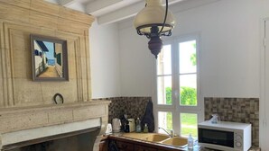 Una cucina con camino in pietra, pensili in legno, un lampadario e vista sull'esterno da una finestra.