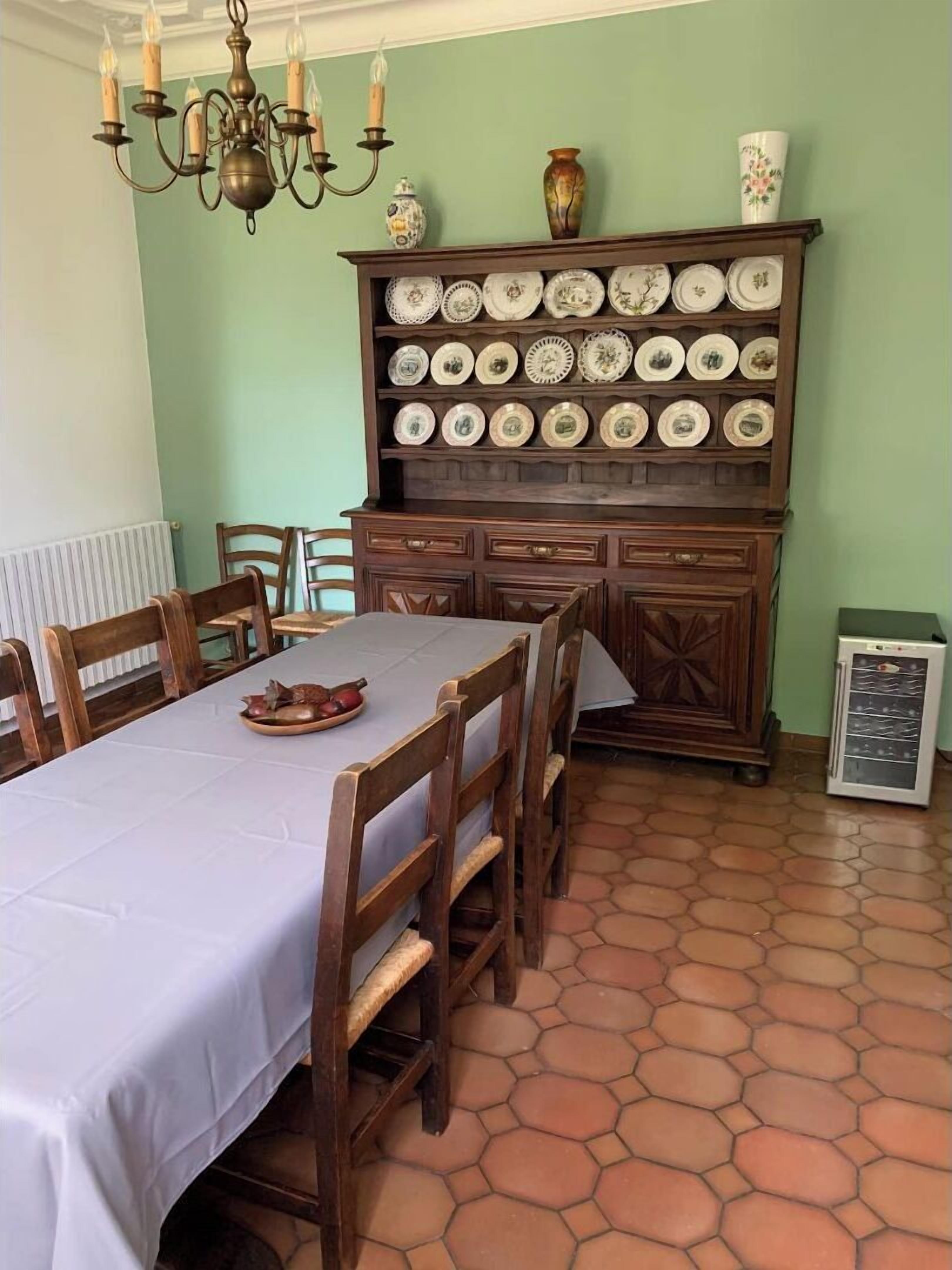 Ein Esszimmer mit einem langen Tisch, Holzsesseln, einer Kristallleuchtre und einer Plateausstellung in einem Holzschrank.