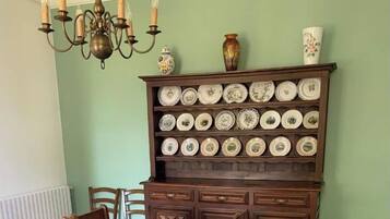 A dining room with a long table, wooden chairs, a chandelier, and a display of plates on a wooden cabinet.