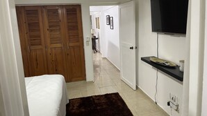 A bedroom with a bed, a ceiling fan, a wooden wardrobe, a TV mounted on the wall, and a bathroom visible through an open door. - Marant's Lodge #2 (Puerto Plata)