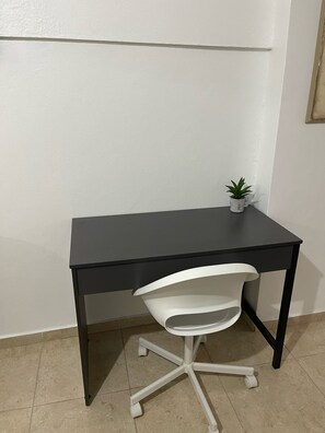 Ein kleiner, dunkelbrauner Schreibtisch mit weißem Stuhl und einem kleinen Blumentopf darauf.