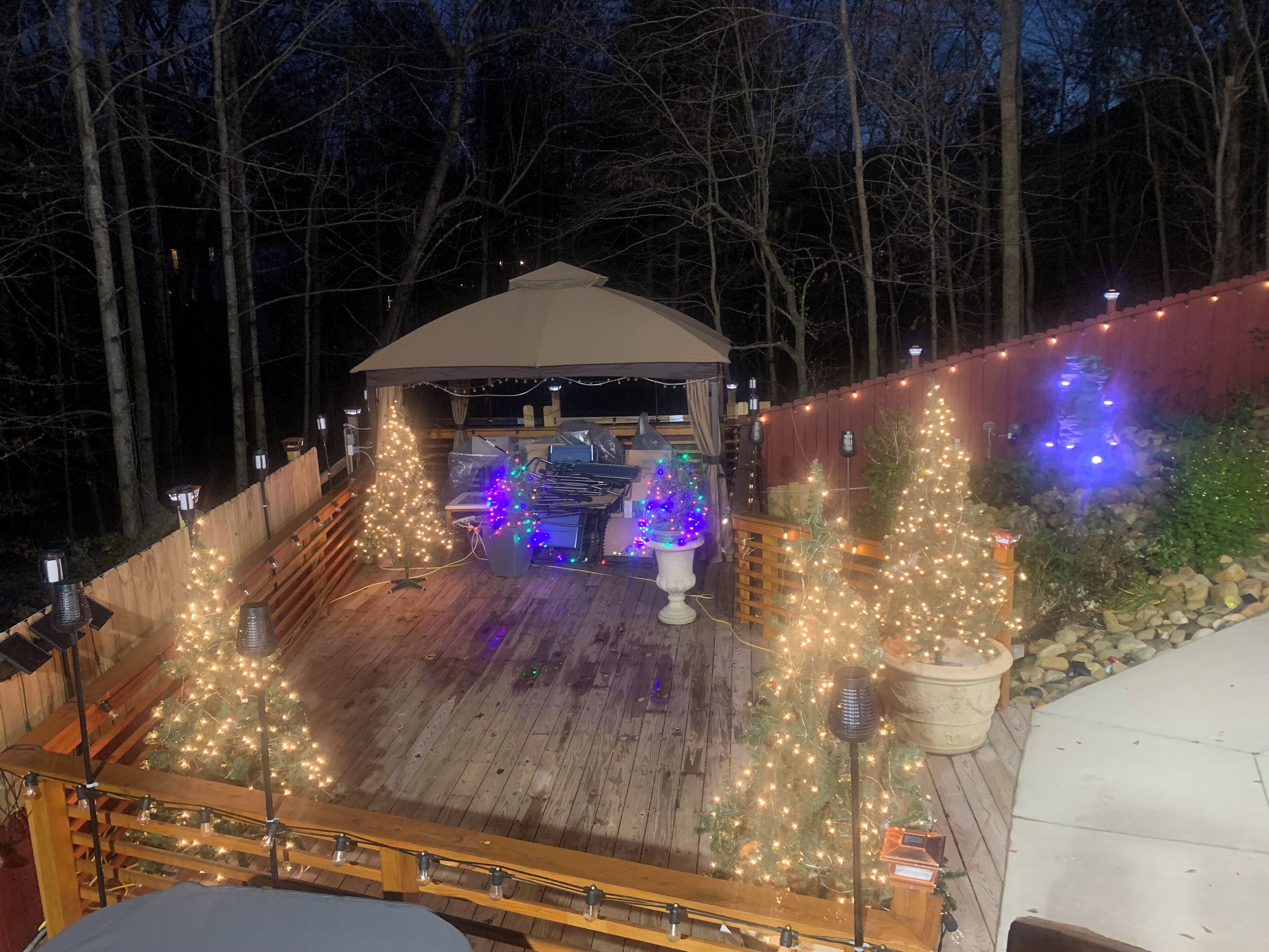A wooden deck with a covered seating area, surrounded by trees and decorated with string lights.