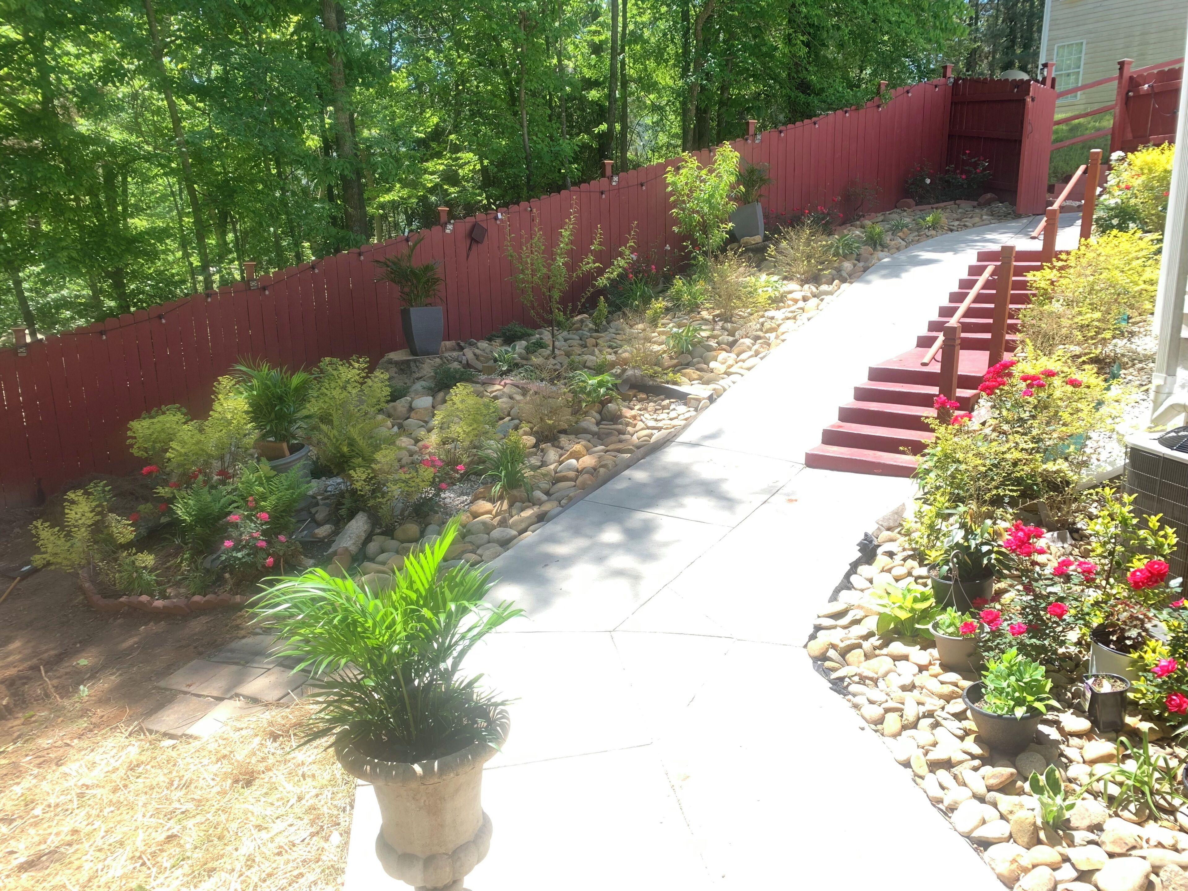 Un chemin de jardin bordé d’une clôture rouge, agrémenté de plantes en pot et d’une bordure en pierre.
