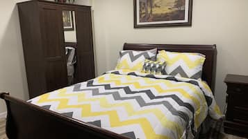 A bedroom with a bed, a wardrobe, a nightstand, a framed picture on the wall, and a potted plant.