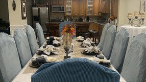 Un comedor con una araña, una mesa preparada para seis personas y una cocina al fondo.