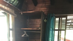 Ein Zimmer mit Holzwänden, Fliesenboden, einem Fenster mit Vorhängen und einem Bett mit einer gestreiften Decke.