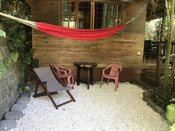 A wooden cabin with a hammock, two plastic chairs, a patterned chair, and a small table. - CASA COLIBRI (Montezuma)