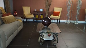 Una sala de estar con un sofá, dos sillones, una mesa de centro y una mesita auxiliar con objetos decorativos.