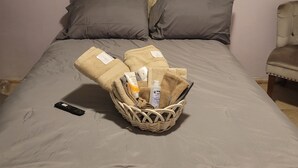 Una cama bien tendida con un cabecero capitonado, dos almohadas y una cesta con artículos de aseo sobre la cama.