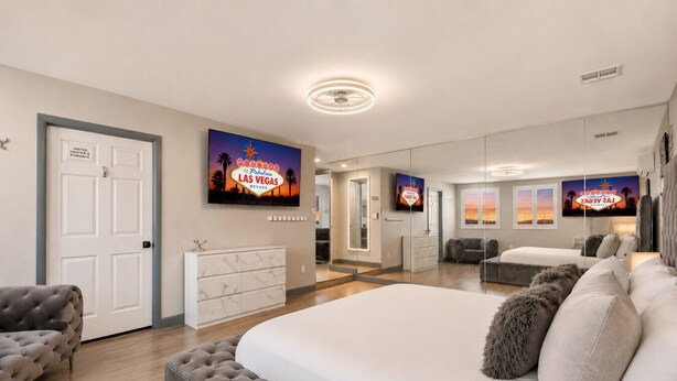 Ein geräumiges Schlafzimmer mit einem großen Bett, einem grauen Sofa und einem Fernseher, der eine Las Vegas Beschilderung zeigt.