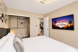 Une chambre dâhĂŽtel avec un lit, un placard, une porte donnant sur une salle de bain et un tĂ©lĂ©viseur fixĂ© au mur qui affiche lâenseigne de Las Vegas.