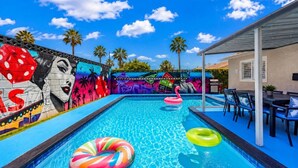 Ein Schwimmbecken mit farbenfrohen Wandmalereien, Liegestühlen und einer überdachten Terrasse.