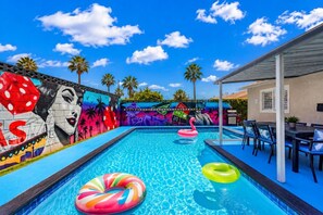 Une piscine agrémentée de peintures murales colorées, de chaises longues et d’un espace patio couvert.