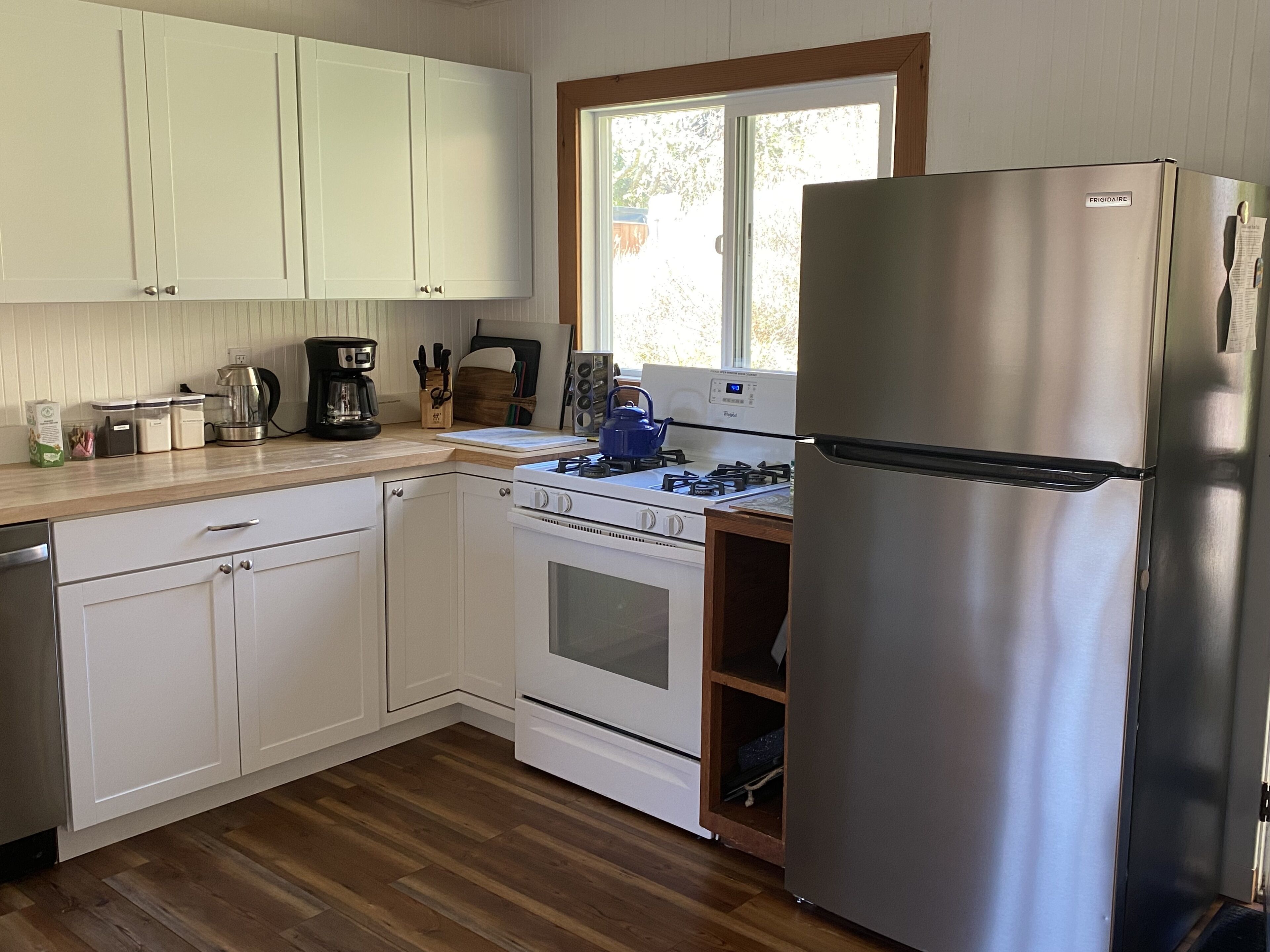 A kitchen with white cabinets, a stainless steel refrigerator, a stove, and a window.
