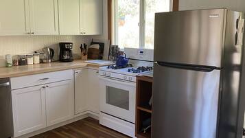 A kitchen with white cabinets, a stainless steel refrigerator, a stove, and a window.