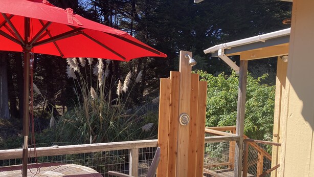 A wooden deck with a red umbrella, a wooden chair, and a table.