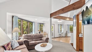 A spacious living room with a large sofa, a round coffee table, and a view of the outdoors through large windows.
