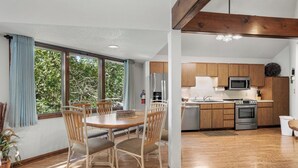 A modern kitchen with wooden cabinets, stainless steel appliances, and a dining area with a wooden table and chairs.
