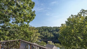 A deck with outdoor seating overlooking a forested area and a body of water.